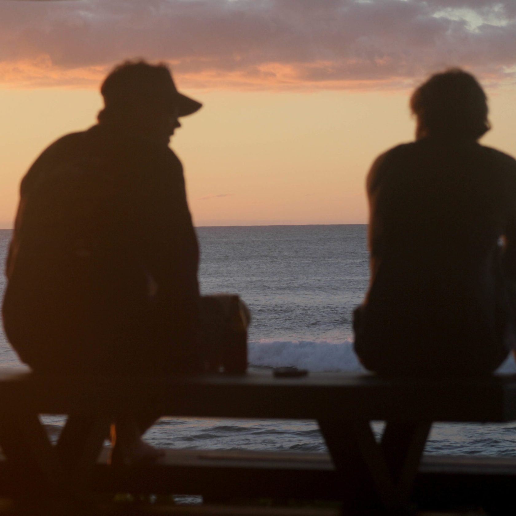 a couple of people that are sitting on a beach looking at the ocean