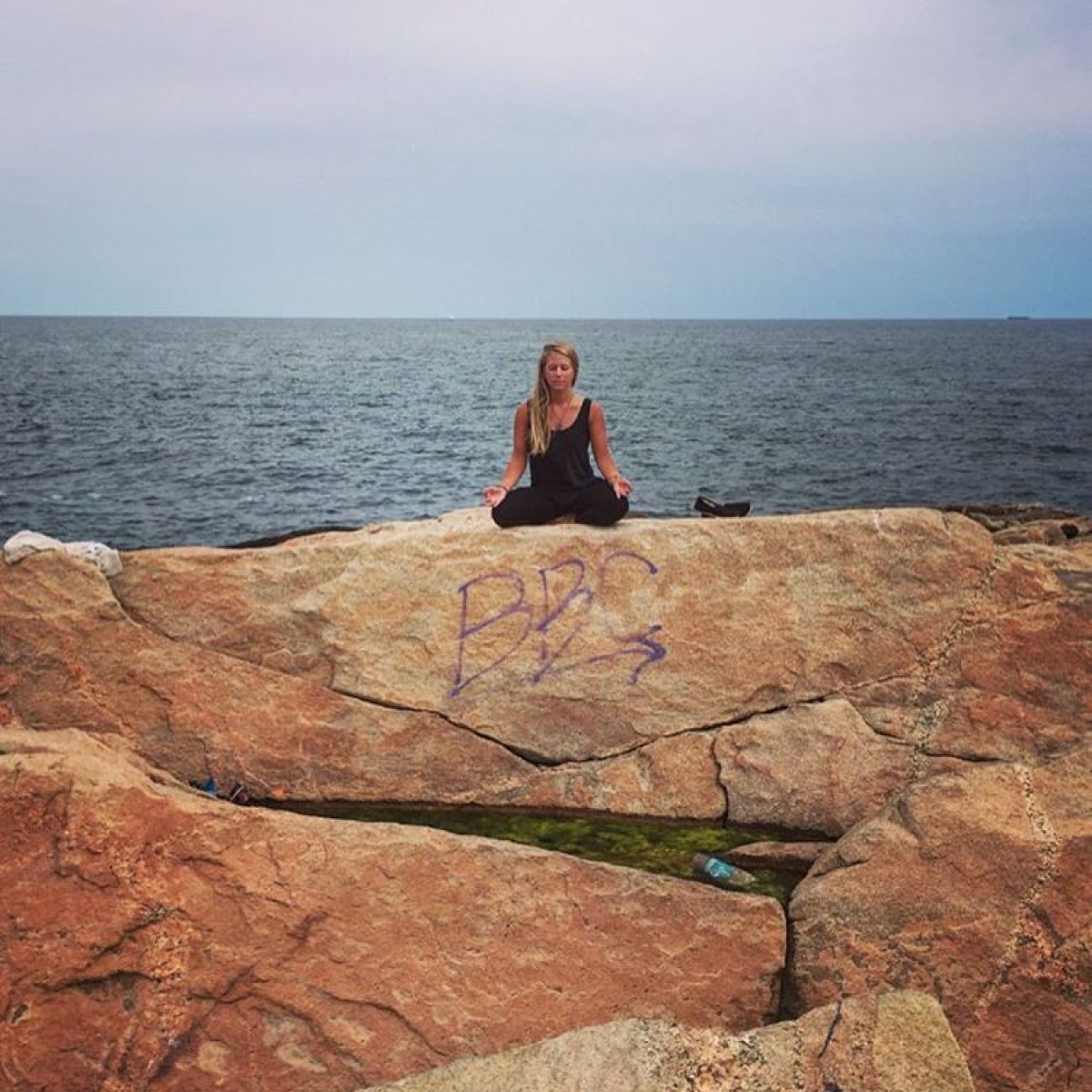 a person sitting on a rock next to a body of water
