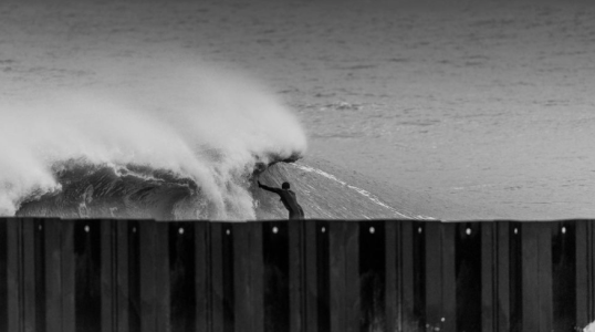 a person riding a wave on top of a wooden fence