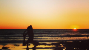 a person walking down a beach with a sunset in the background