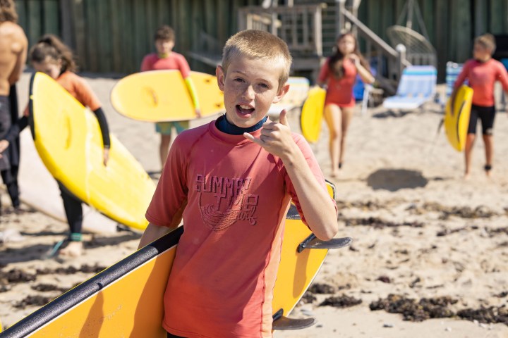 a young boy carrying a surfboard on top of a sandy beach