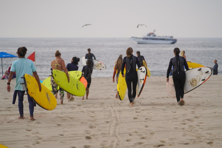 a group of people walking on a beach holding a surf board