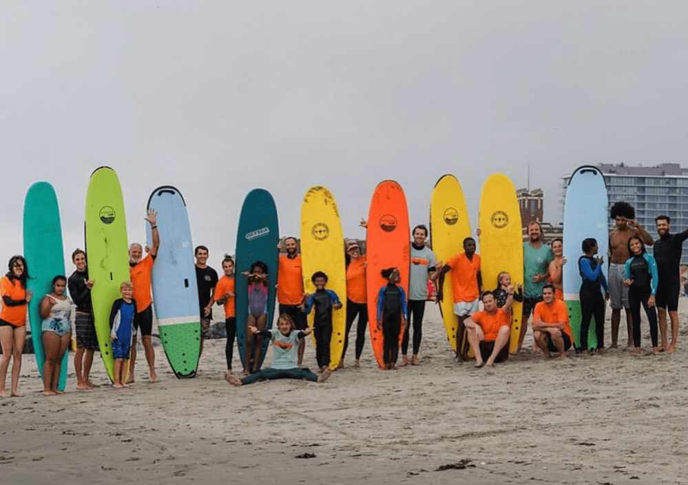 a group of people standing on a beach holding a surfboard