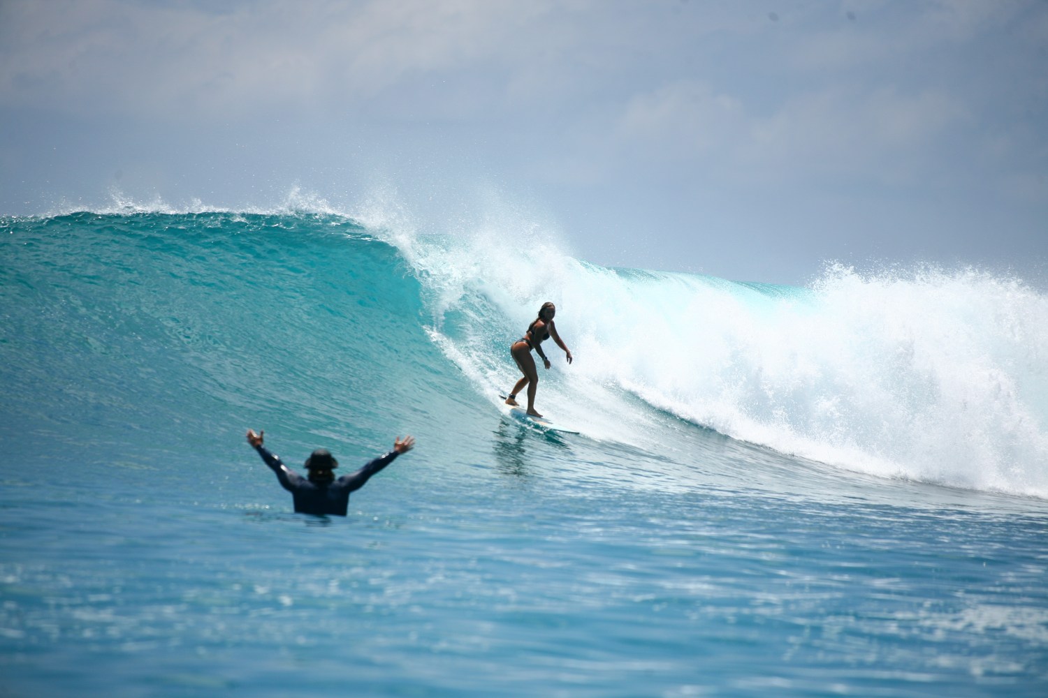 Surfer rides a wave while another person watches in the foreground.